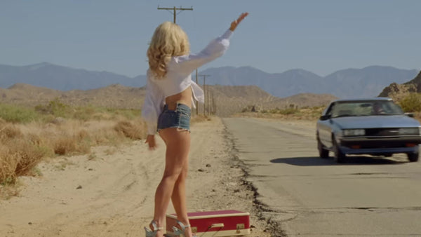 Sabrina Carpenter trying to flag down a car to hitchhike.