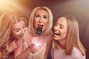 Three girls singing into a wired microphone